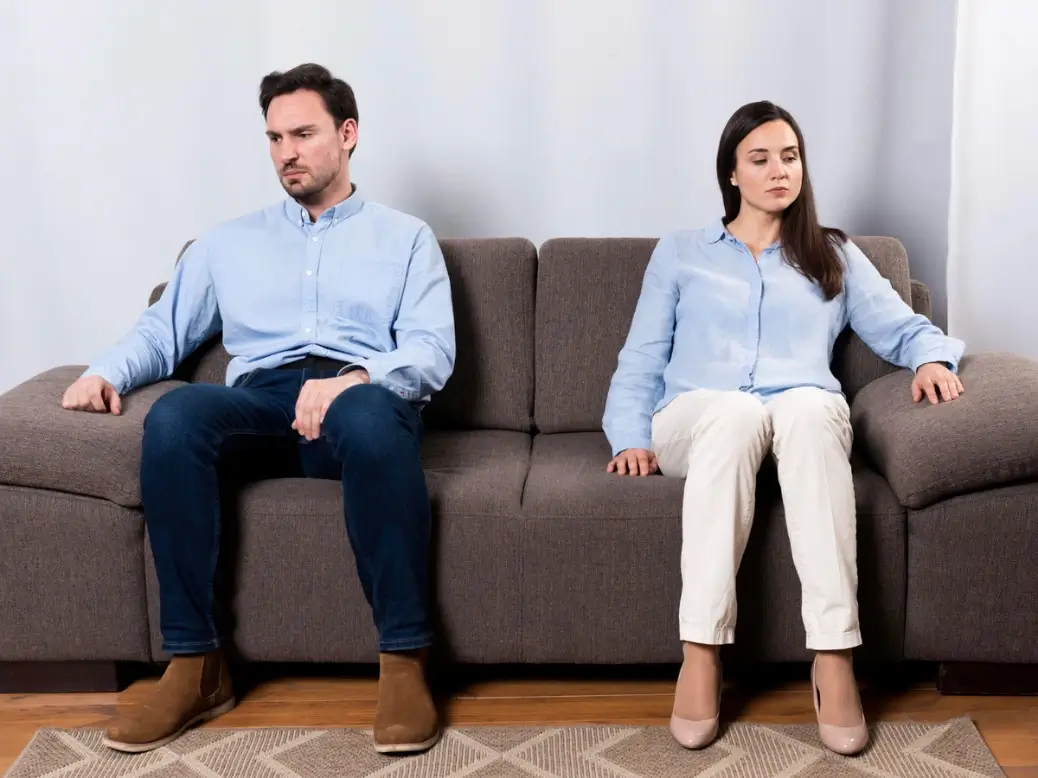 A couple sitting apart looking emotionally distant, representing relationship burnout