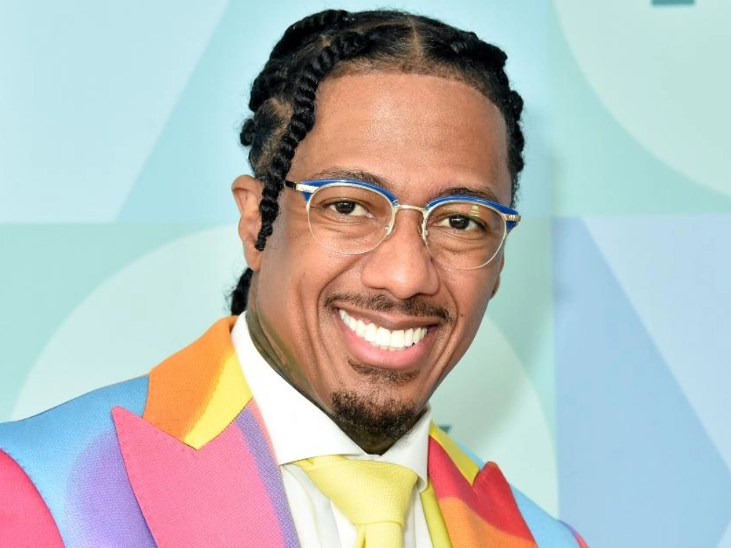 Nick Cannon smiling in a suit with TV host mic, symbolizing his $100 million net worth in 2025